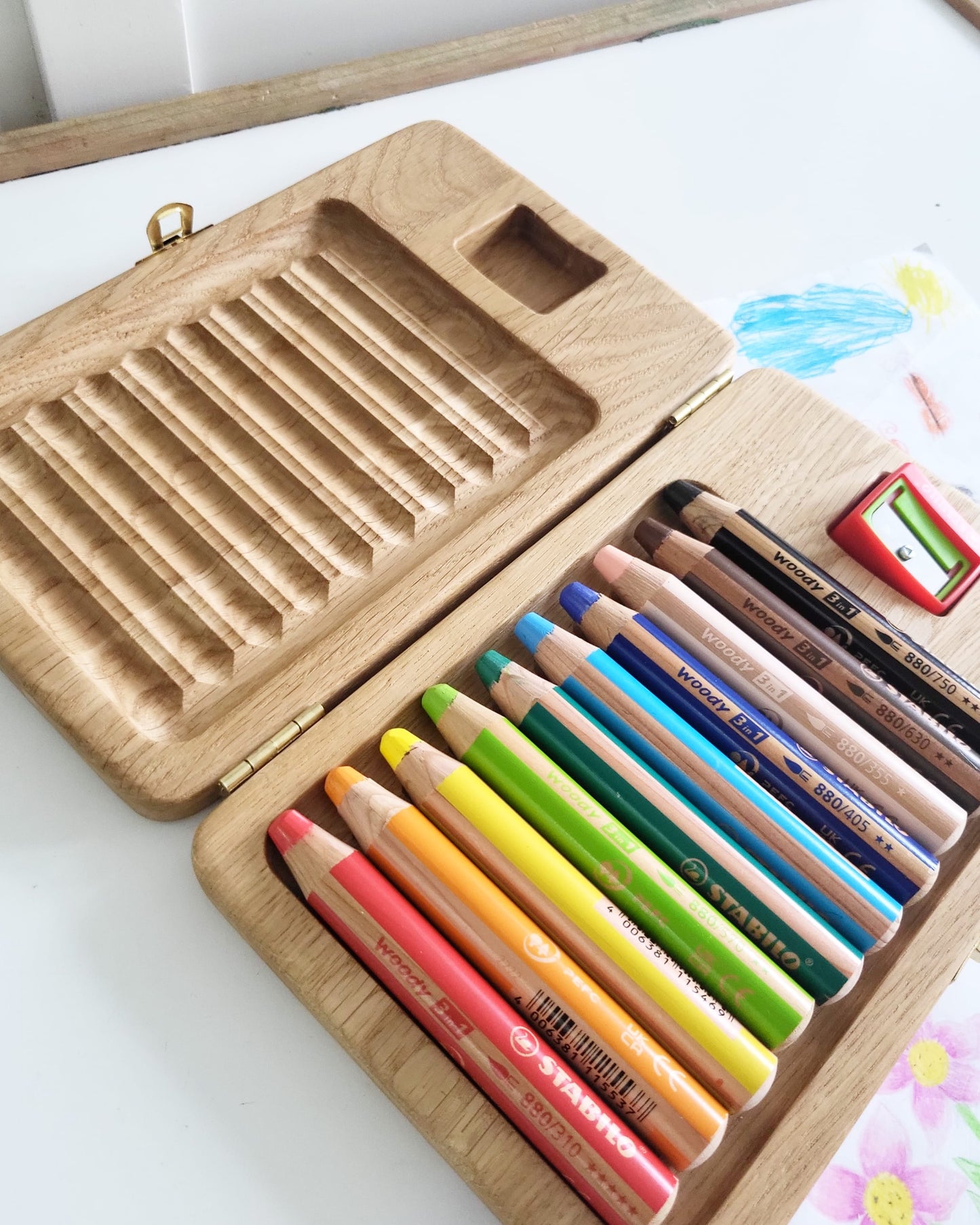 Wooden pencil case with colored pencils and a sharpener on a white surface.