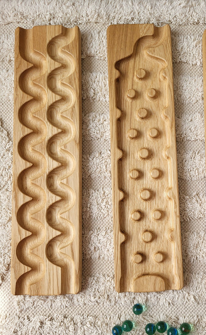 Three natural wood decorative blocks with carved grooves and holes, arranged vertically on a textured white surface next to a small pile of green and blue marbles.