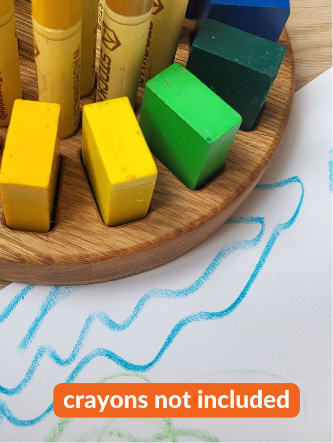 Colorful crayons and blocks on a wooden tray with a piece of paper underneath.